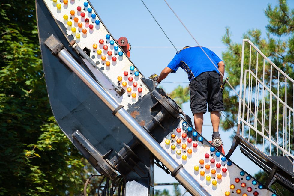 Worker inspecting colorful lights on an amusement ride structure.