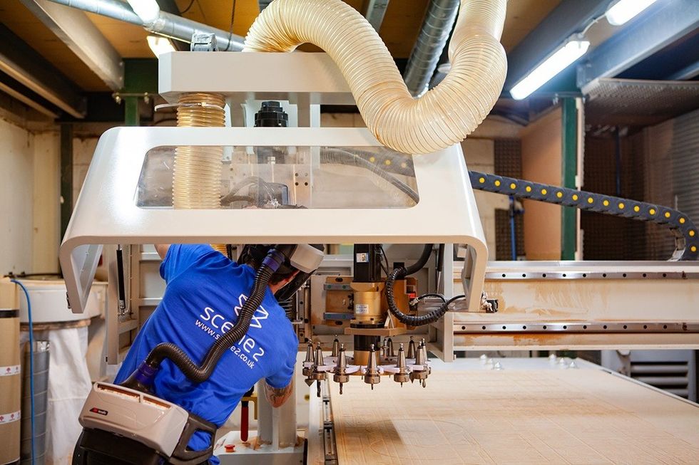 Worker operating a large CNC machine in a workshop with overhead ventilation.