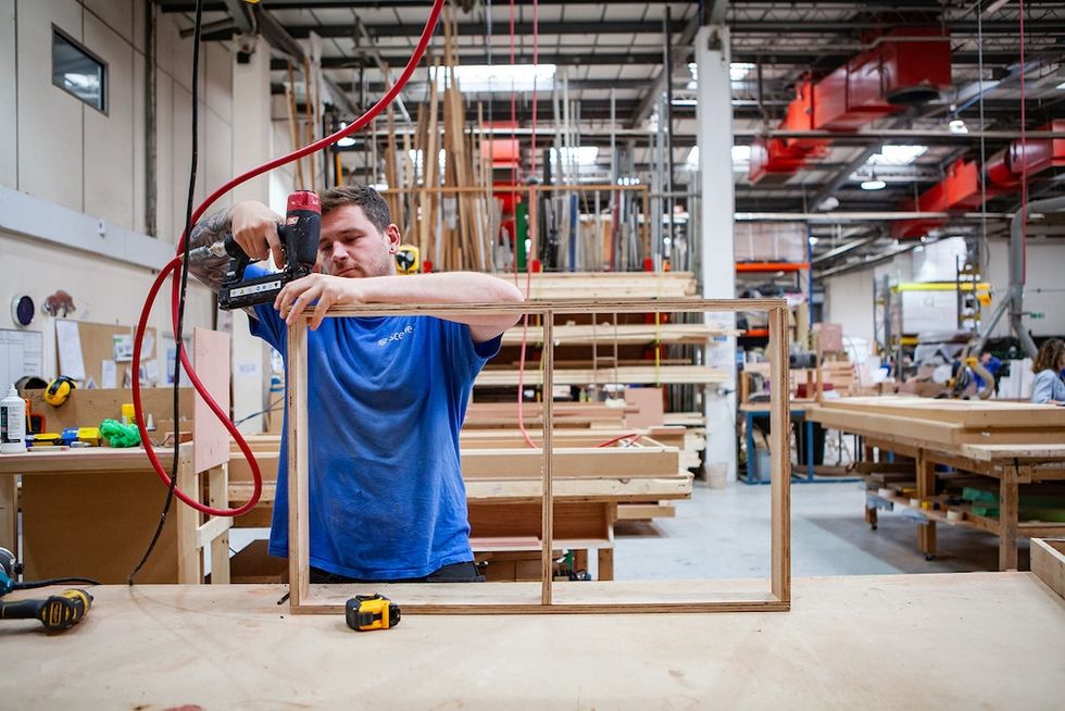 Worker using a nail gun to build a wooden frame in a carpentry workshop.