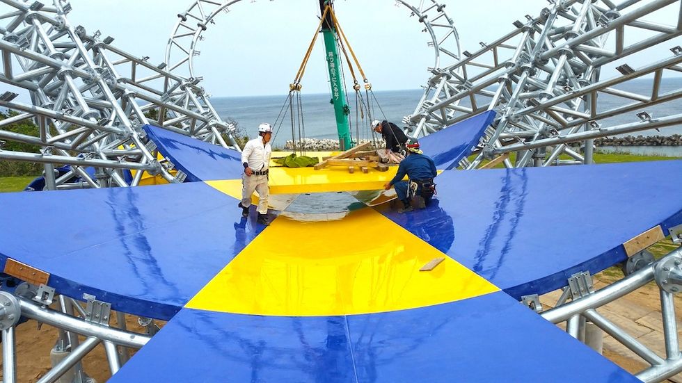 Workers assembling a large blue and yellow WhiteWater slide near the ocean.