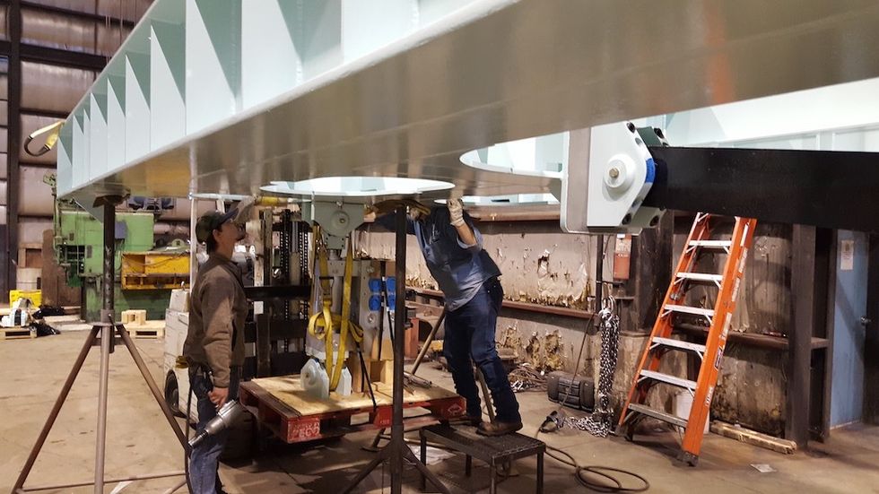 Workers assembling a large metal structure in an industrial workshop.