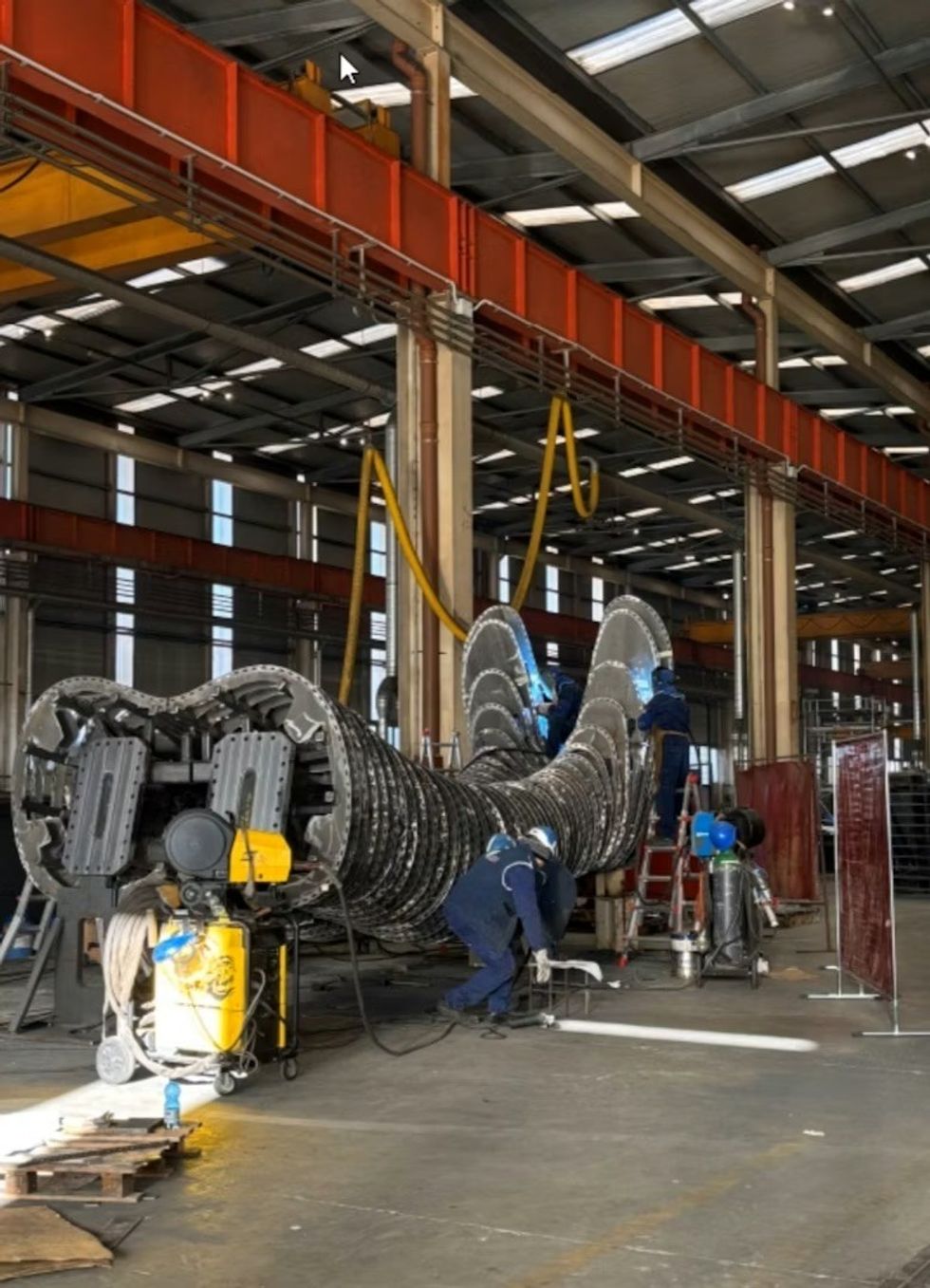 Workers assembling large metal Giant sections in an industrial facility.