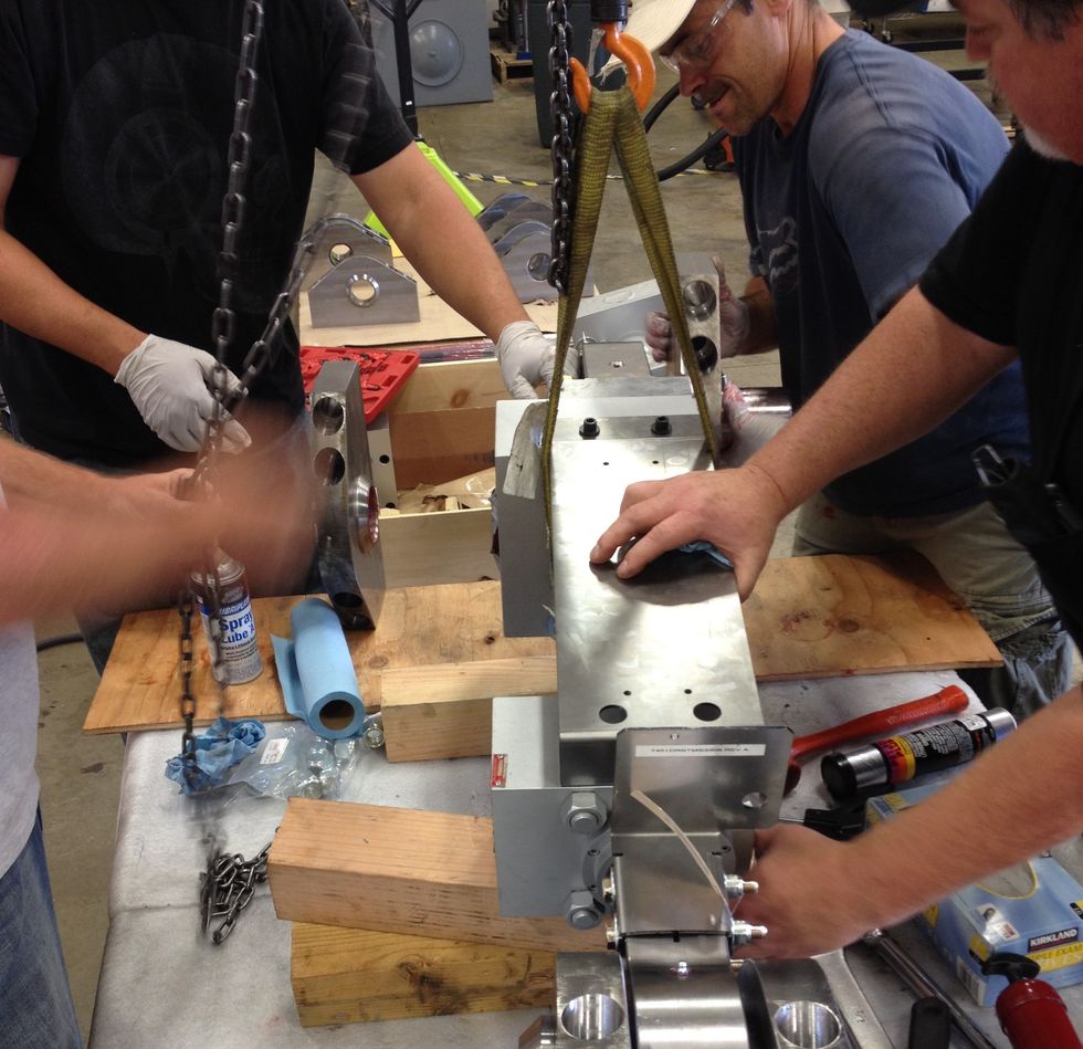 Workers assembling large metal machinery with chains and tools.