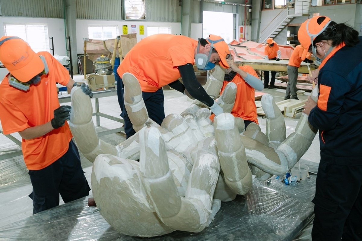 Workers in orange gear crafting a large hand sculpture in Pico Play's workshop in Vietnam.