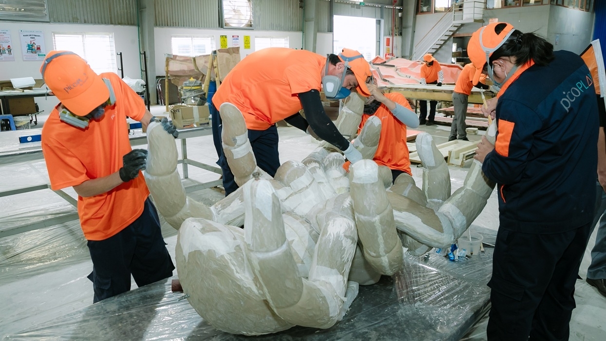 Workers in orange gear crafting a large hand sculpture in Pico Play's workshop in Vietnam.