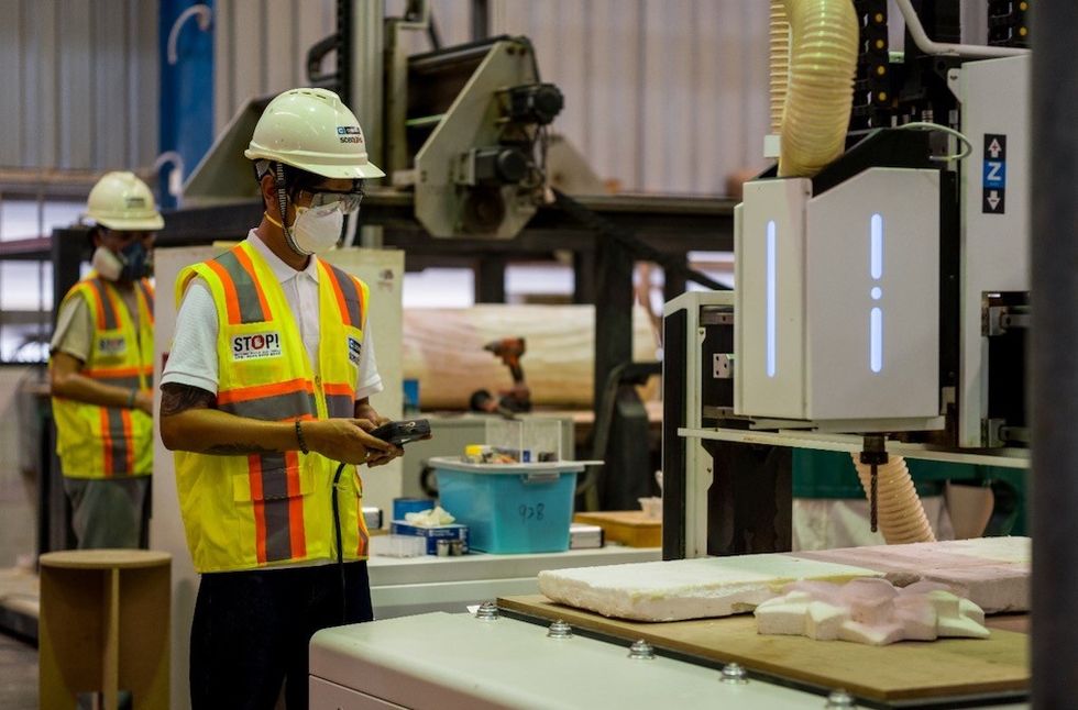 Workers in safety gear operate machinery in a factory setting.