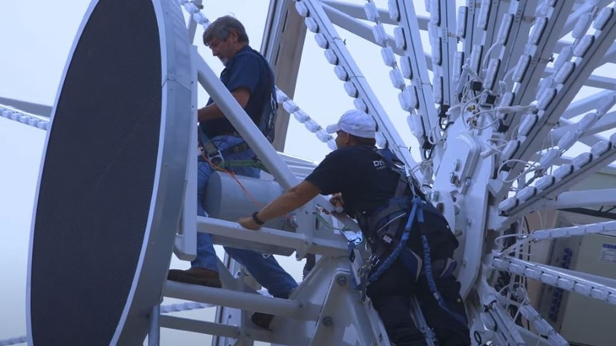Workers inspecting large Chance Rides Ferris wheel mechanism in safety harnesses.