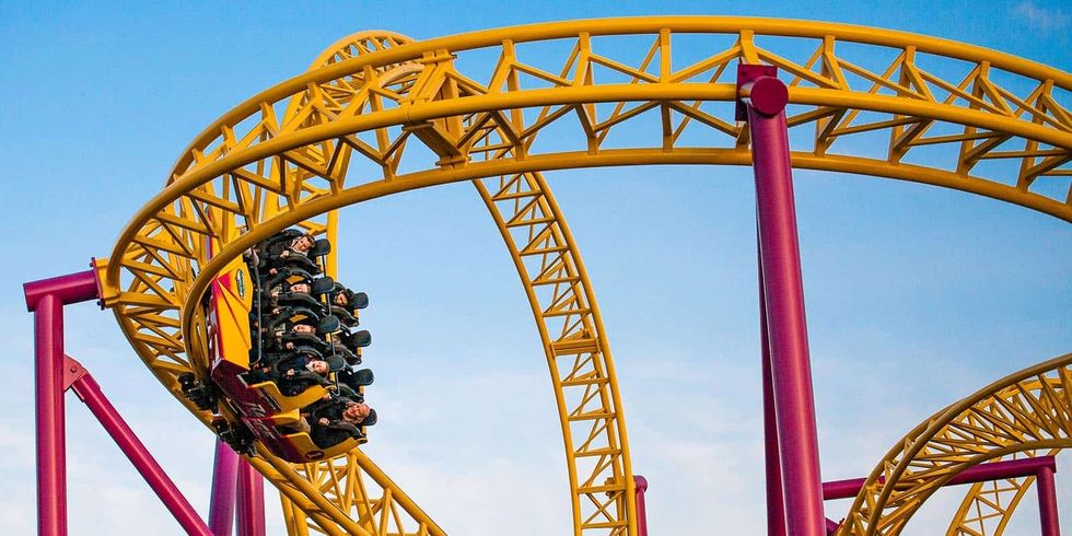 Yellow and pink roller coaster with riders upside down on loop.