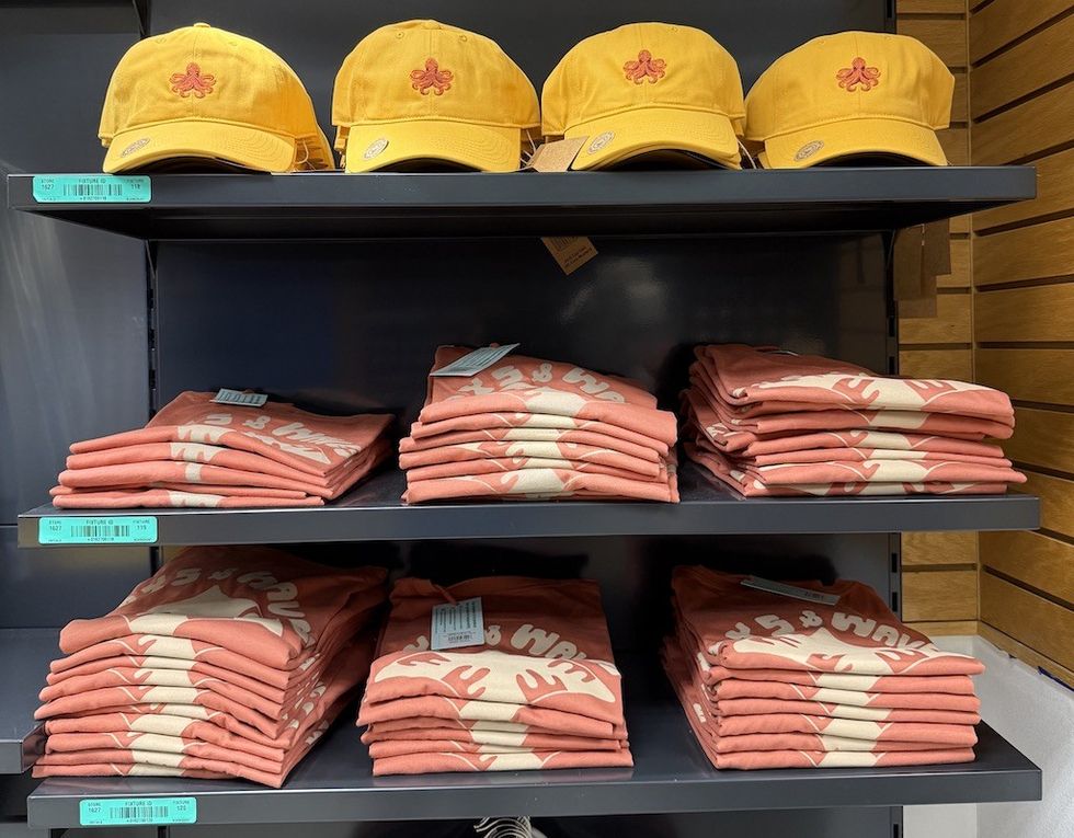 Yellow caps and folded pink shirts neatly displayed on shelves with inventory tags