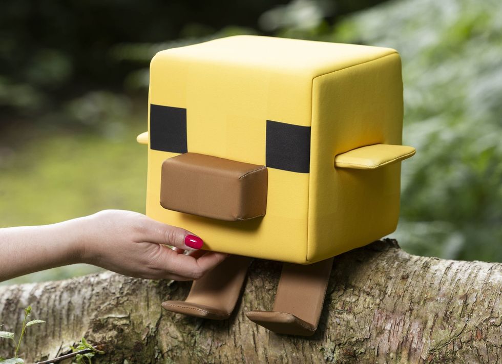 Yellow cube-shaped Minecraft bird on a log, with a hand touching its side.