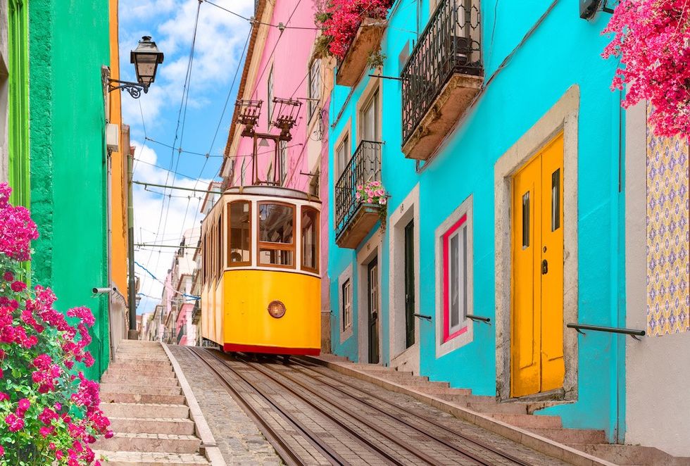 Yellow electric tram on a street with colorful houses and flowers on the balconies - Bica Elevator going down the hill of Chiado in Lisbon, Portugal.