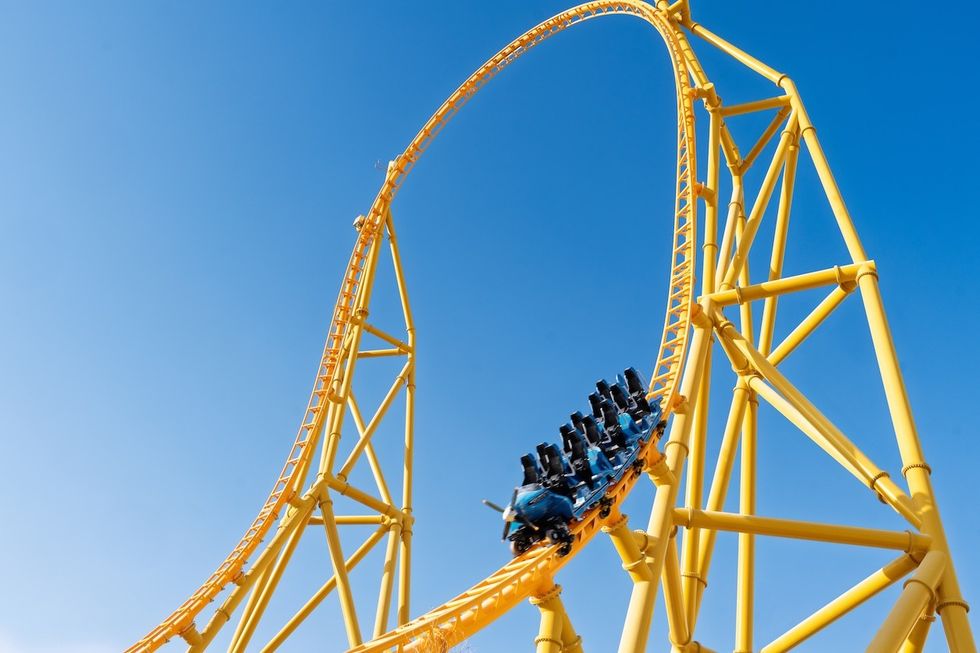 Yellow roller coaster with a loop against a clear blue sky.