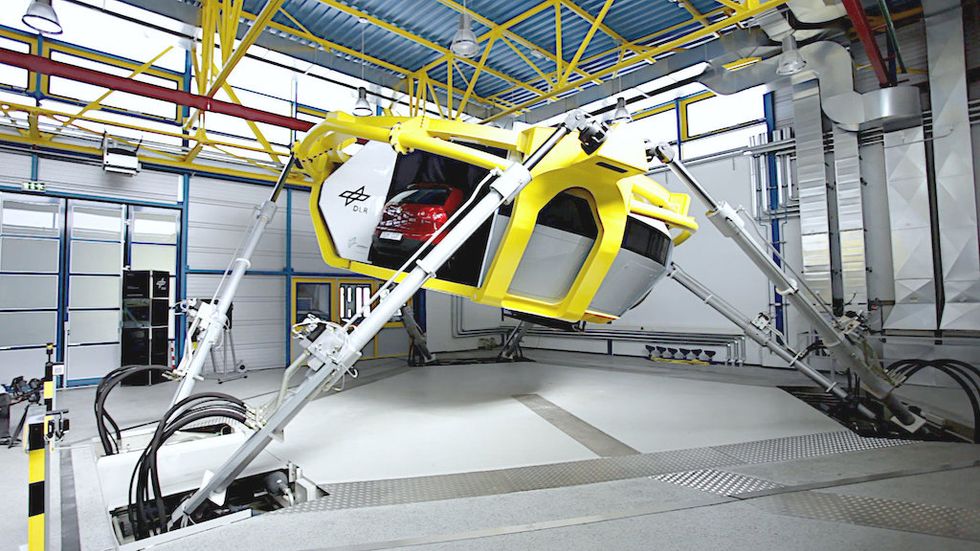 Yellow vehicle simulator with adjustable arms in a high-tech lab setting.