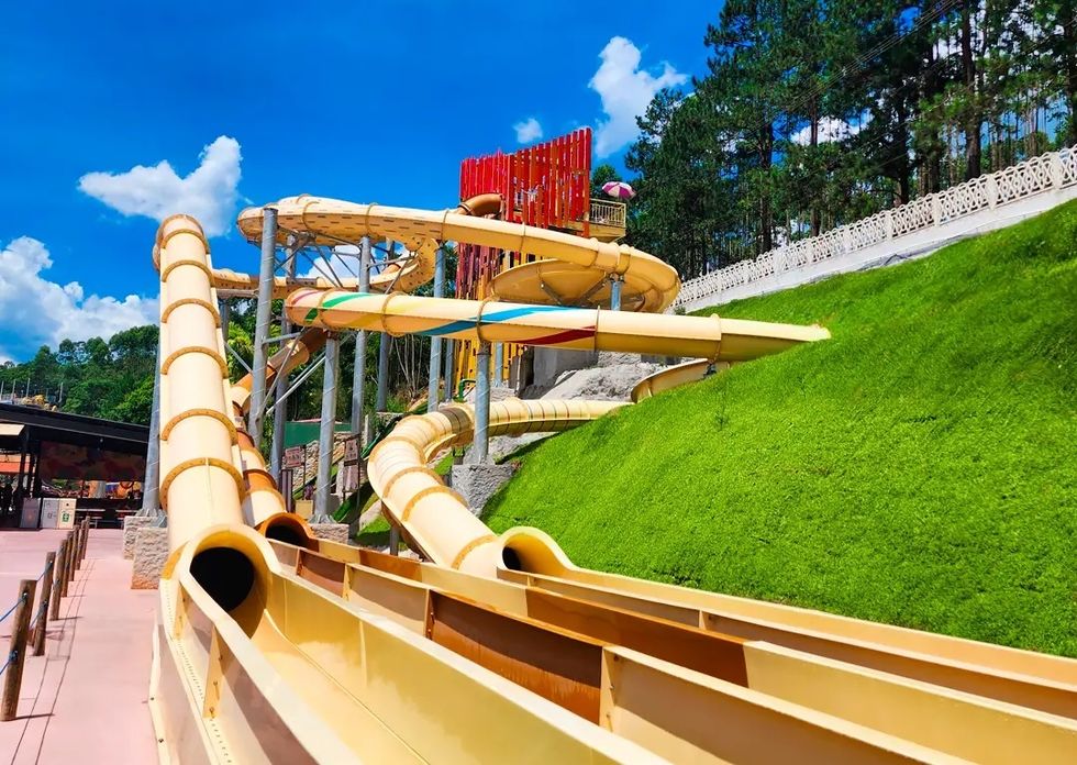 Yellow water slides at Magic City with loops and turns on a sunny day, surrounded by green grass and trees.