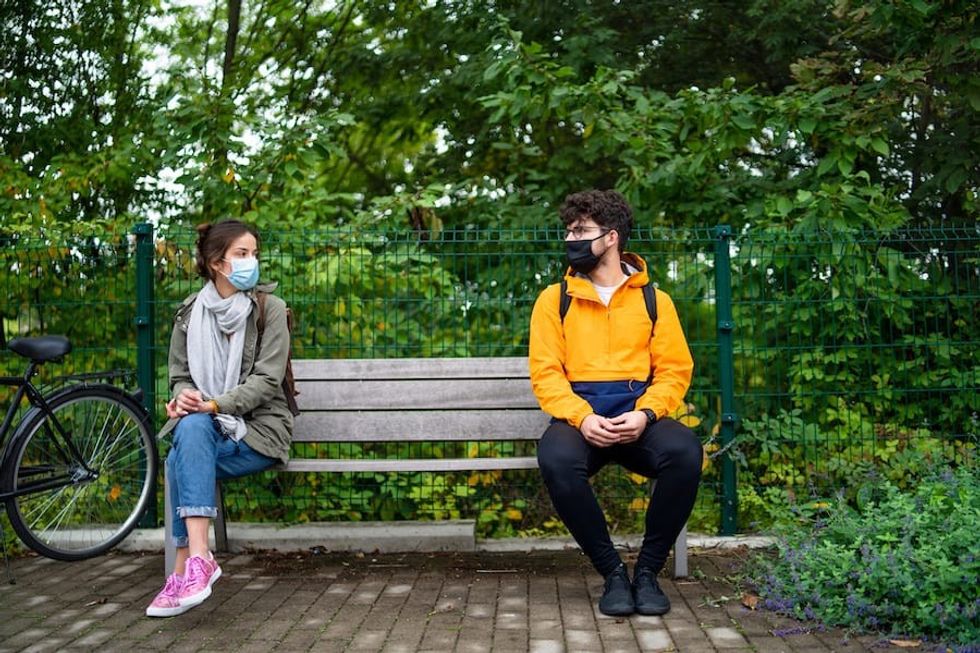 Young people talking on bench outdoors in town. Coronavirus and safe distance concept shared experience