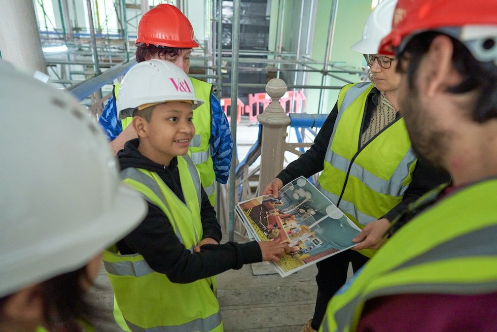 Young V&A Youth Collective members in hard hats and vests discussing plans at Young V&A construction site.