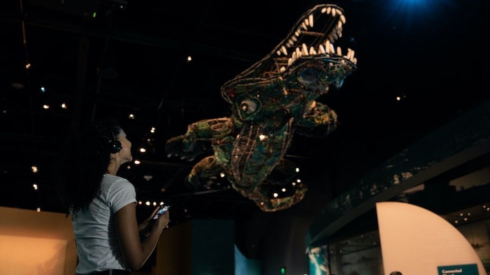 Young woman in museum looks up at crocodile sculpture