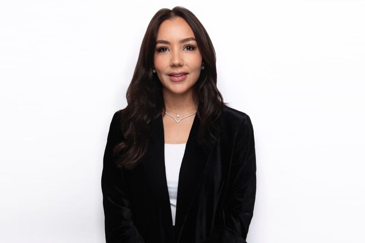 Zeina Dagher in a black blazer against a white background, smiling and facing the camera.
