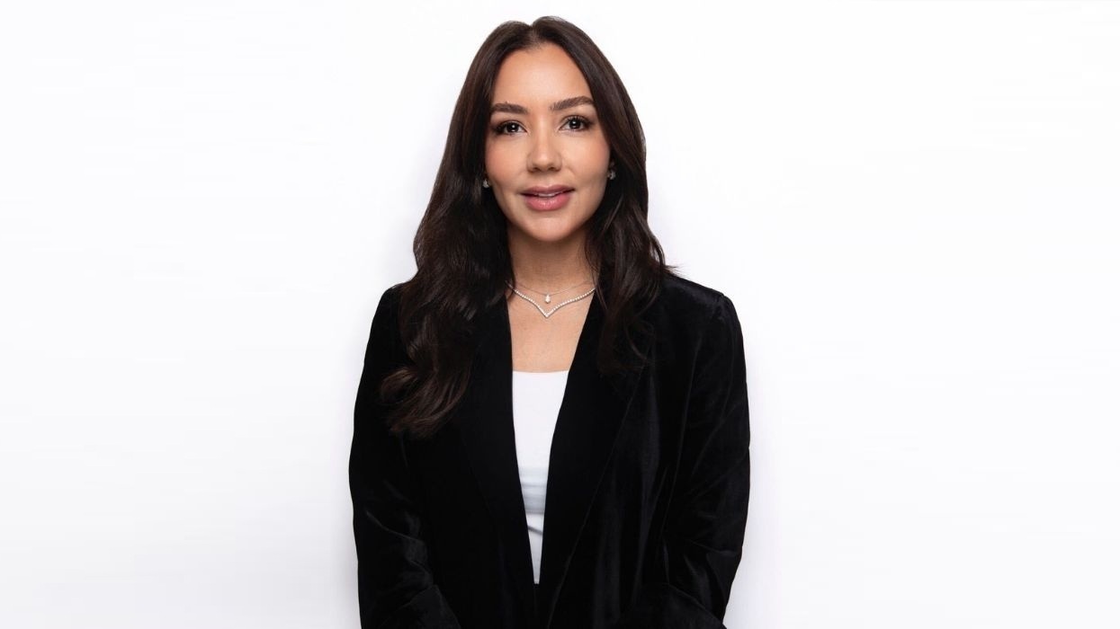 Zeina Dagher in a black blazer against a white background, smiling and facing the camera.