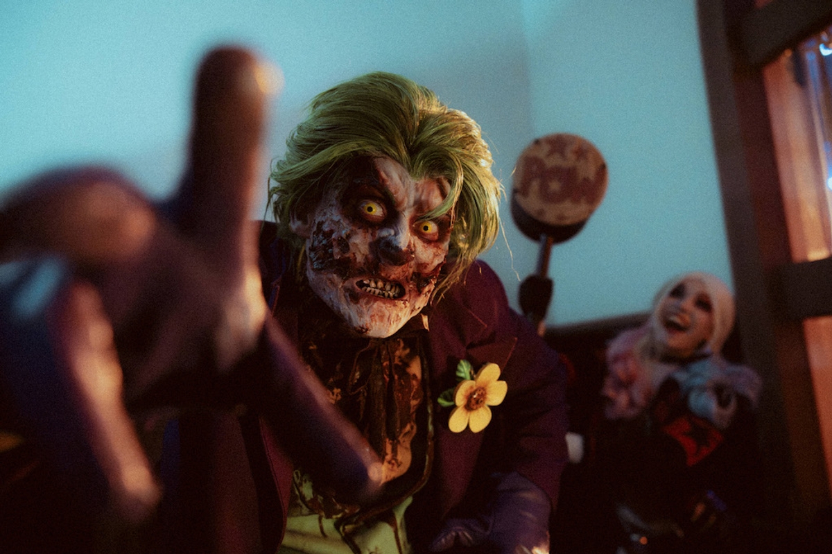 Zombie-like character in a green wig, with another person laughing in the background.