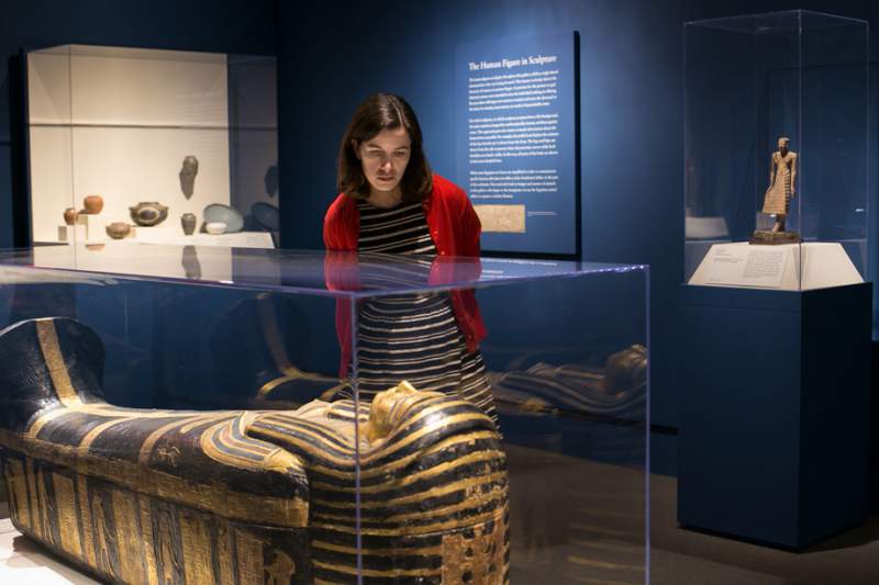 woman views egyptian mummy in case at saint louis art museum