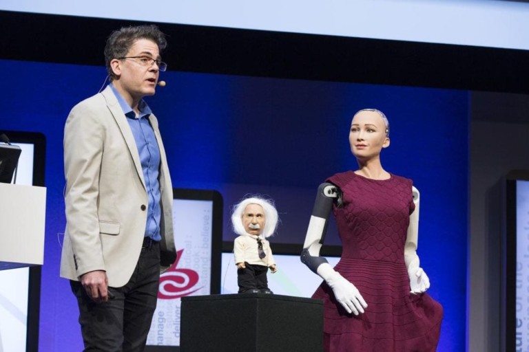 Speaker at IBC with mini figure of Einstein and female robot