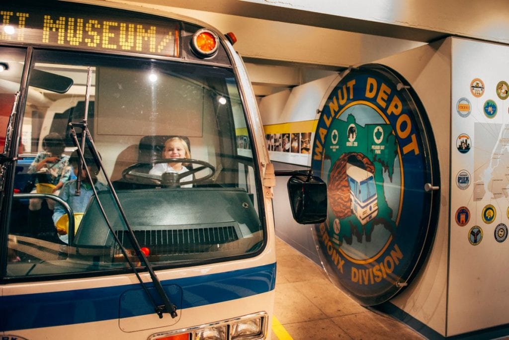 2 children on the bus and 1 child on the bus driver's seat in the New York Transit Museum