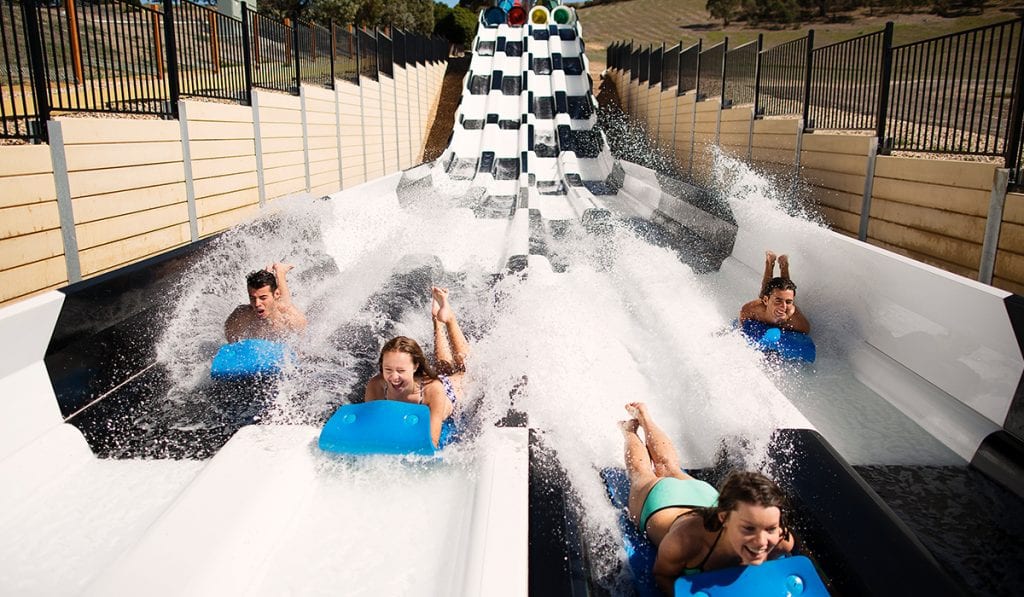 Four individuals racing on a blue mat, head first on a black and white Kraken Racer