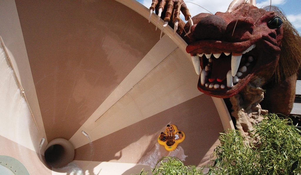 Four riders on a clover raft at the peak of a funnel water ride about to reach teh top where a model monster is waiting