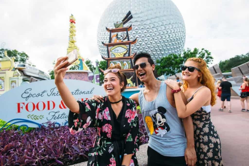 Three guests taking a photo in front of Epcot's International Food and Wine Festival 2018 signage