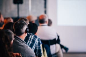 Man with headphones using earphone for reel time translation and Audience people sitting rear at the business seminar on the white screen in Conference Hall.