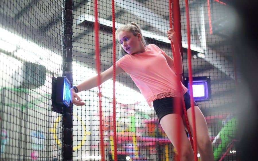 Girl touches wristband to TAG Active touchpoint on ropes course from iplayco showcasing at Amuseument Expo 2020