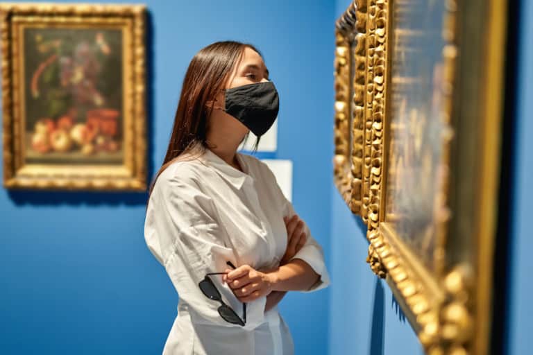 Woman visitor wearing an antivirus mask in the historical museum looking at pictures.