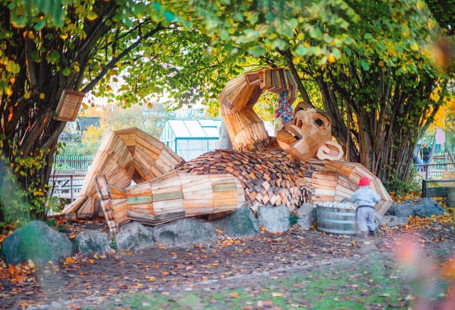 Recycled troll sculpture lying on side by trees from Imagine Exhibitions new exhibit