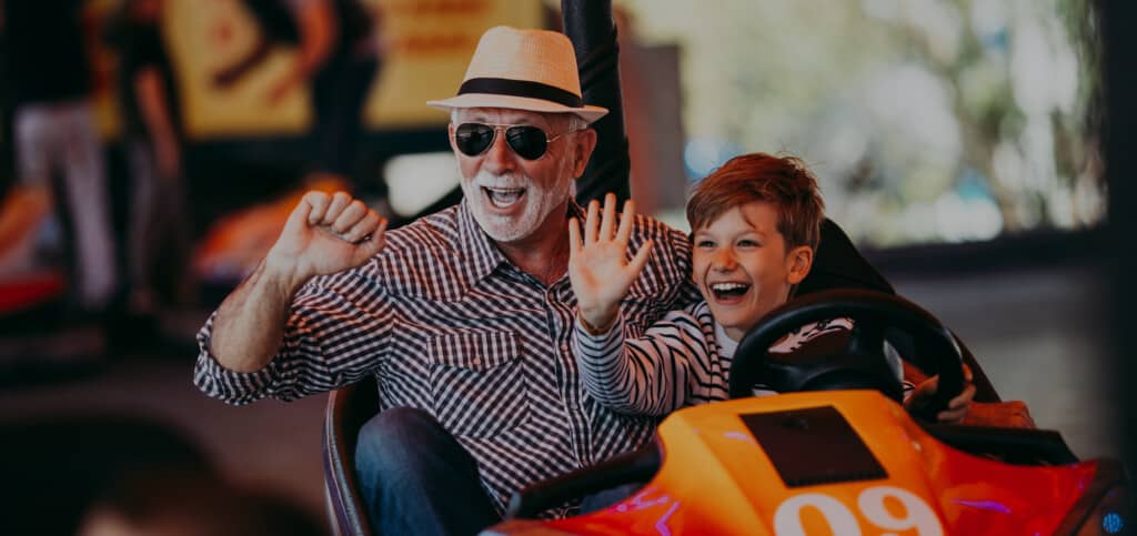 Grandfather and grandson having fun and spending good quality time together in amusement park. They enjoying and smiling while driving bumper car together.