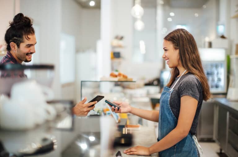 Male customer paying with NFC technology with smartphone at coffee shop. , Man paying for his order in restaurant by mobile phone while bringing it near payment machine in hand hands on female cashier. smeetz