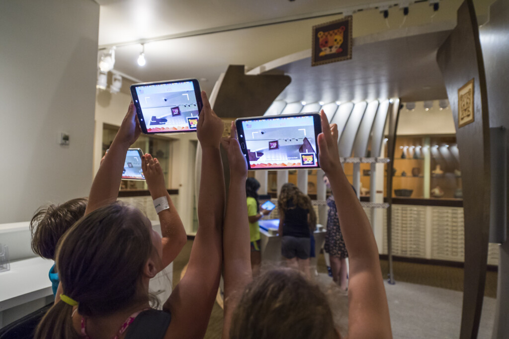 children hold tablets up to museum exhibition