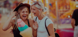 Shot of happy female friends in amusement park eating cotton candy. Two young women enjoying a day at amusement park.