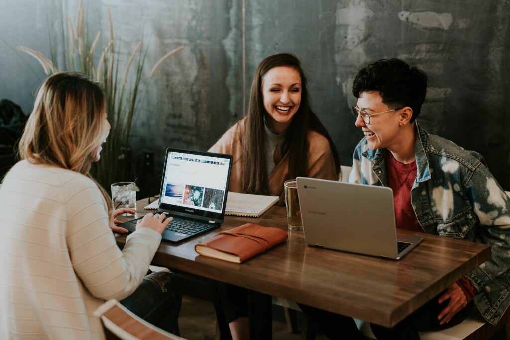 Three young people smiling, using laptops around a table in a modern office environment