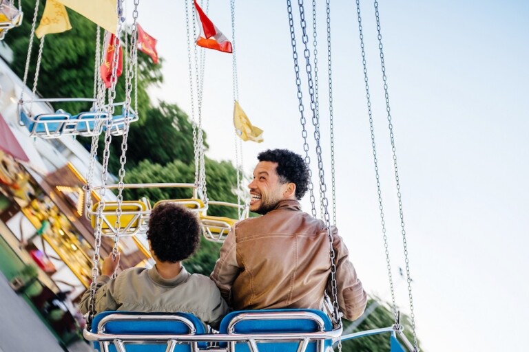 Father And Son Riding Swing Set At Fun Fair