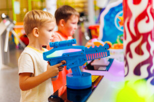 Happy kids playing a shooting game on slot machines at an amusement park.